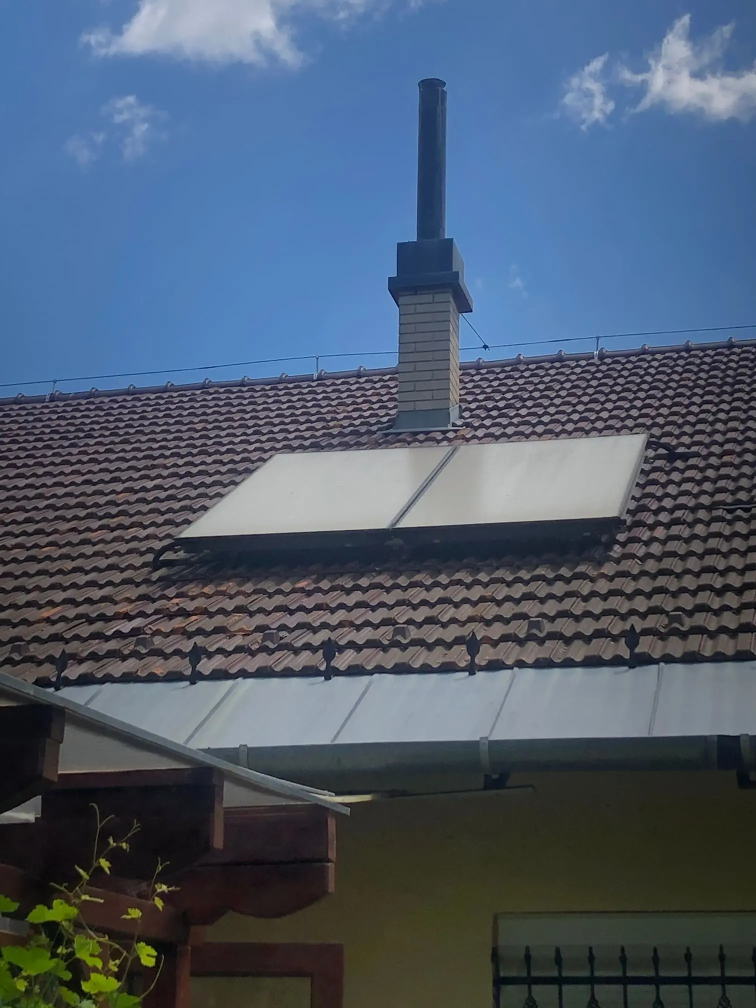 Két síkkollektor cserépfedésű családi ház tetején, a kémény mellett